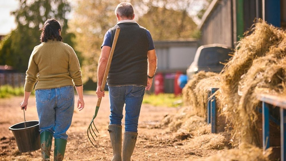 Viel éleveur et jeune éleveuse près d'un bâtiment