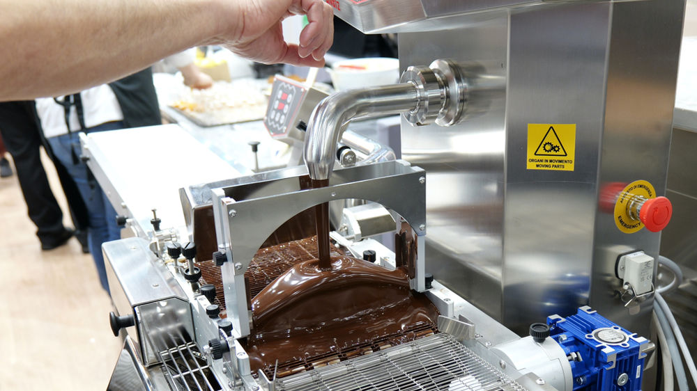 L’enrobeuse forme un rideau de chocolat sous lequel passent les produits.