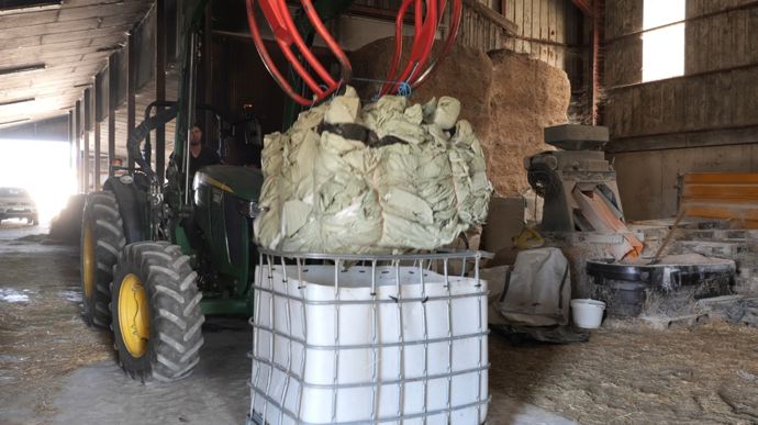 Les bottes de film d'enrubannage sont compressées avec le grappin de l'hydro-fourche du tracteur, ficelées, puis retirées du cubi.